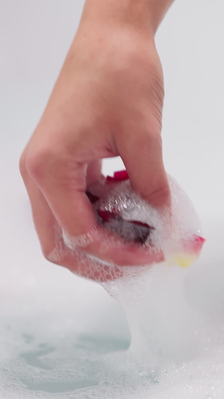 여자는 은 물에서 장미 잎자루를 잡습니다. 여자는 욕조에서 자연 신선한 꽃을 특징으로하는 향기있는 거품 목욕을 즐니다. 스파 살롱 경험