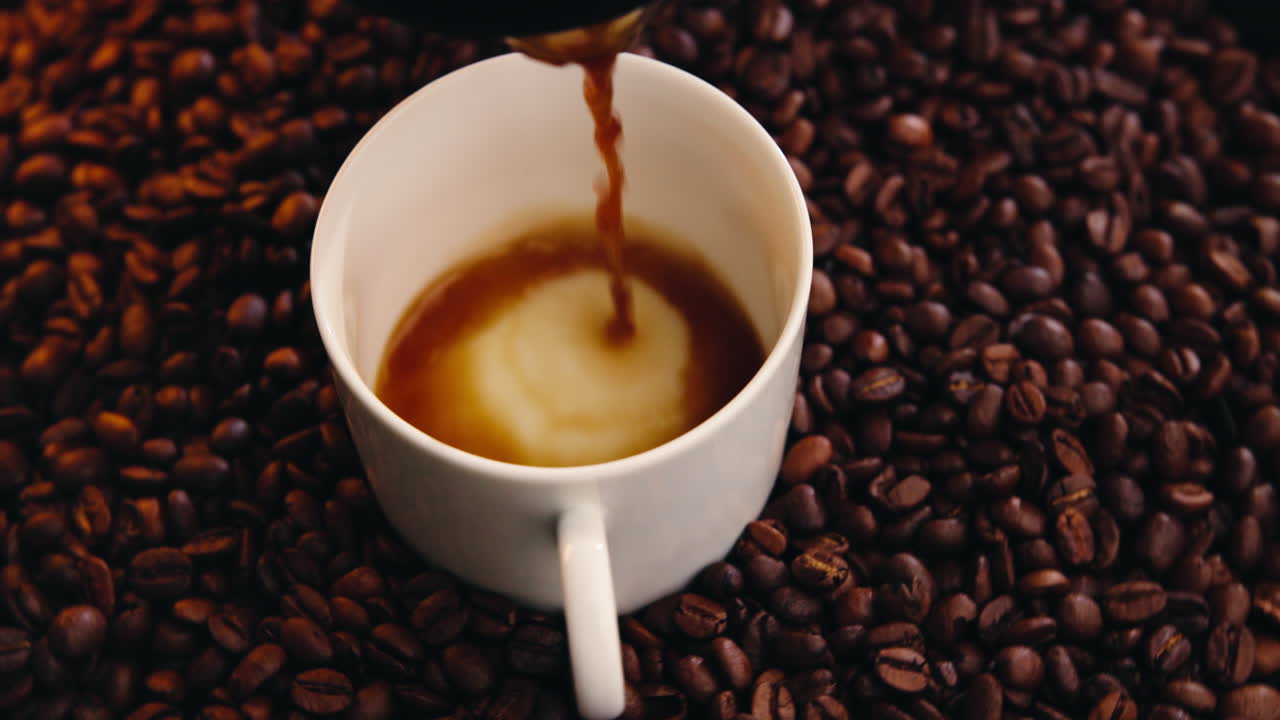 Café recién hecho vertiéndose en una taza blanca sobre granos tostados