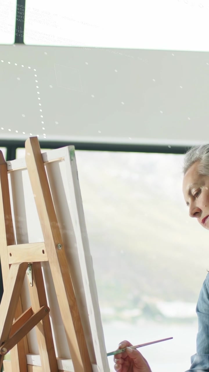 Vertikal video: Pensel kommer ind, kvinde læner sig ved staffeli ved persienne, mens lyset glimter, laver kunststrøg