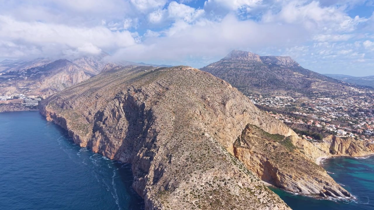 İspanya, Calpe yakınlarındaki Morro de Toix burnu seyir noktası, turkuaz Akdeniz'e inen dramatik kayalık uçurumları, sahil kasabası ve dağ fonunu gösteriyor.