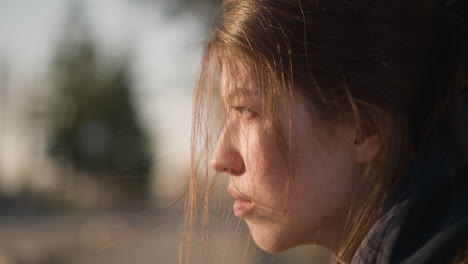 un primer plano de una chica con un abrigo marrón, con su cabello cubriendo parcialmente su cara. parece llorosa y perdida en sus pensamientos, su expresión refleja un profundo sentido de tristeza e introspección