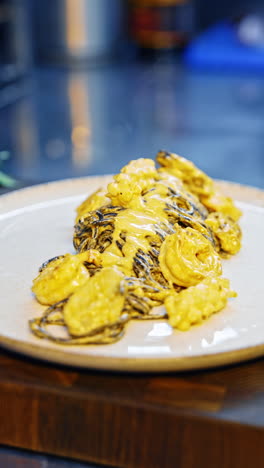 tasty delicious black pasta with seafood on the plate. cook pours some more sauce on top of the dish. close up. vertical video.