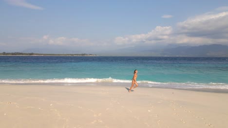 girl in bikini running by the ocean on sandy tropical beach in gili meno,indonesia