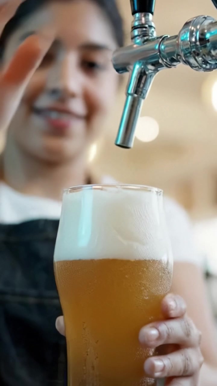 Un barista esperto versa con maestria una birra sapientemente preparata in un bicchiere, mostrando schiuma spumosa e un'invitante carbonazione in una vivace atmosfera da birrificio.