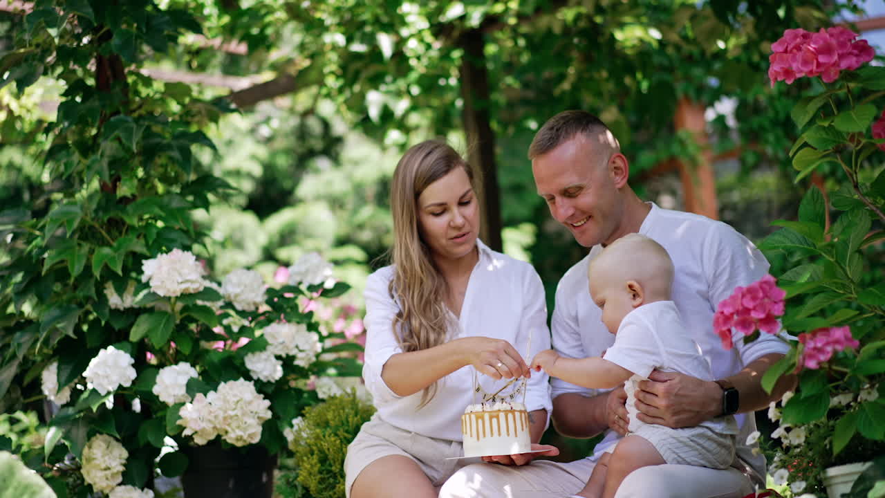 Beautiful Caucasian family of three celebrating the first anniversary of their child. Cute baby boy tries to get a cake in mom's hands.