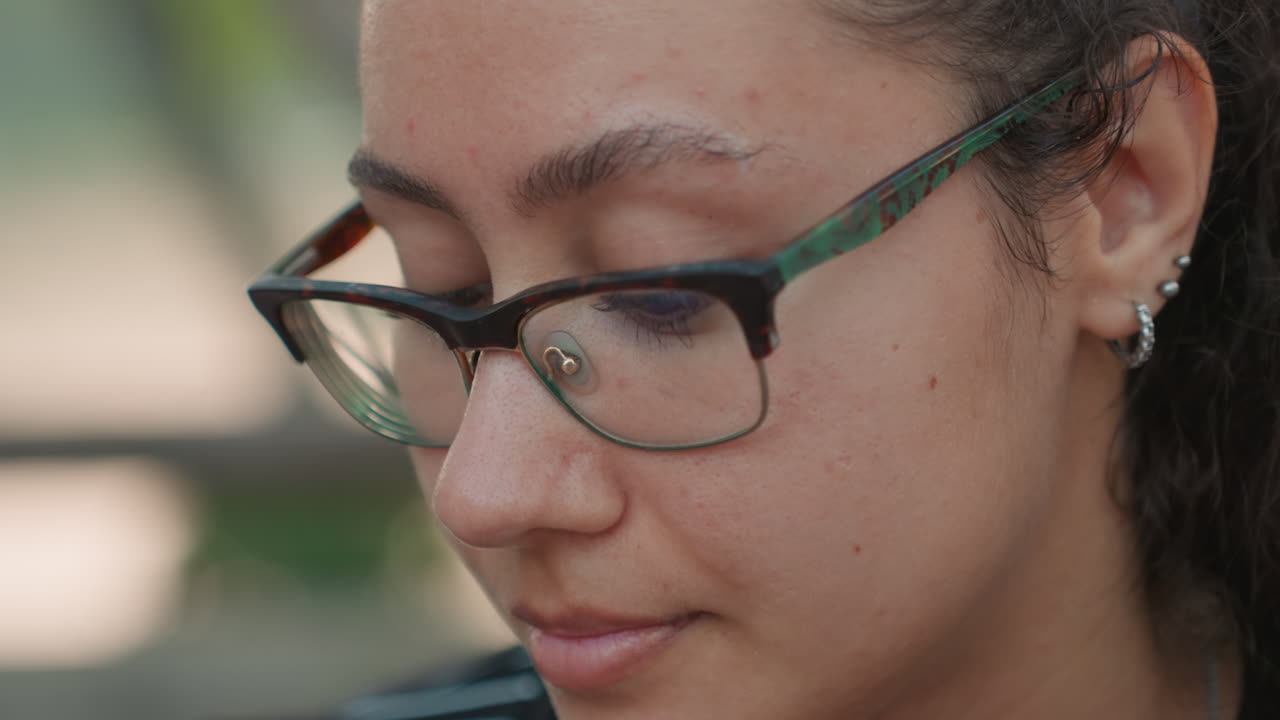 Retrato de mujer concentrada. Primer plano de mujer con pecas al aire libre. Imagen íntima de mujer con gafas en un banco de parque. Toma detallada de mujer pensativa con pecas y gafas con luz natural.