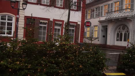 row of christmas trees with twinkling lights in a german market square with a red hotel in the background at a festive christmas market in europe