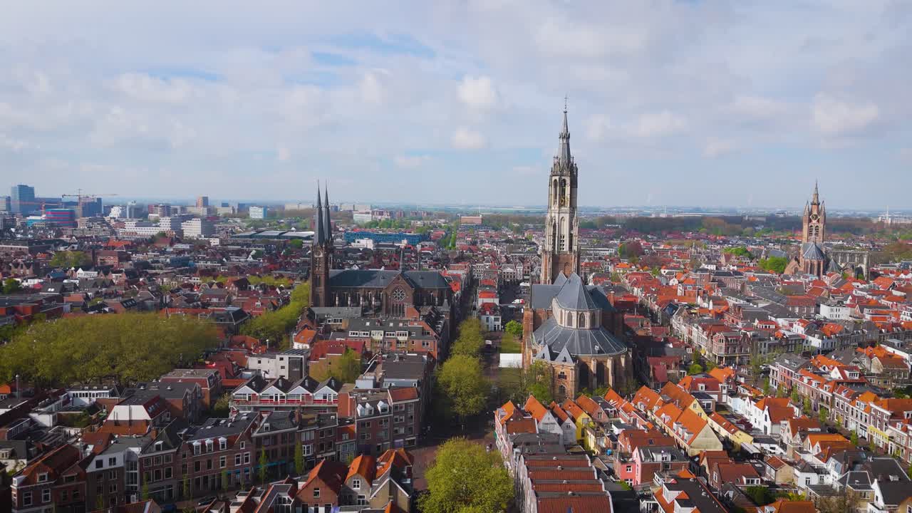 Elevated drone view of the towering Nieuwe Kerk in Delft, dominating the red-roofed cityscape below. Captures the blend of medieval Dutch charm and modern skyline surroundings.