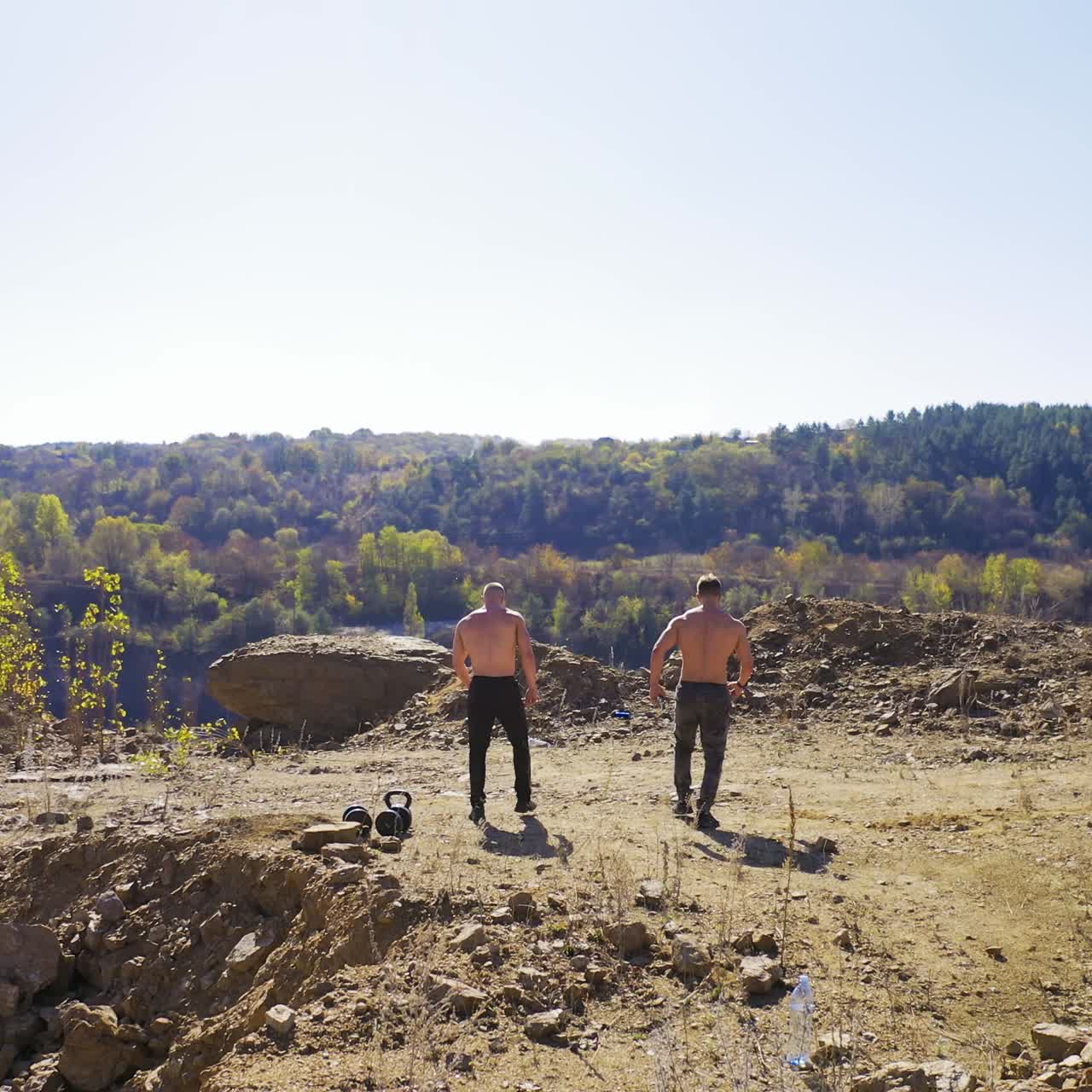 Backside view of two athletes training among nature. Sportive shirtless men with muscular body on the top of the hill. Aerial view.