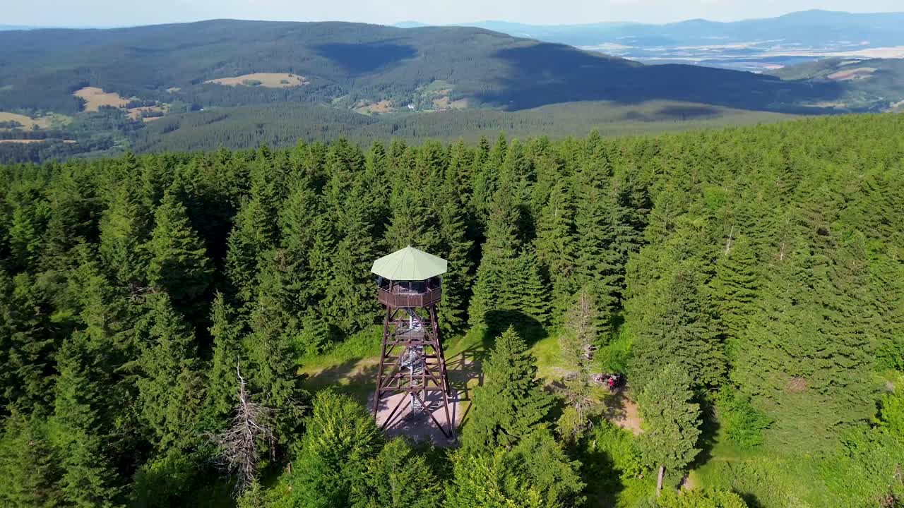 Drone view as it flies over the trees and rotates around and near the lookout tower on the mountains with the valley in the background