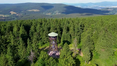 Drone-view-as-it-flies-over-the-trees-and-rotates-around-and-near-the-lookout-tower-on-the-mountains-with-the-valley-in-the-background