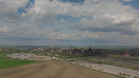 Old-industrial-complex-showing-multiple-smokestacks-surrounded-by-agricultural-fields,-on-a-sunny-clear-day,-tracking-wide-shot