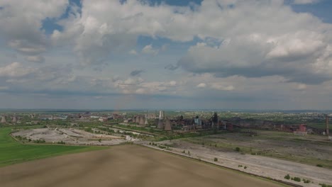old industrial complex showing multiple smokestacks surrounded by agricultural fields, on a sunny clear day, tracking wide shot