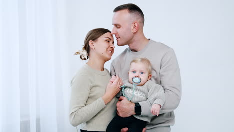 man holding a baby kisses his wife on the forehead. portrait of a happy caucasian family.