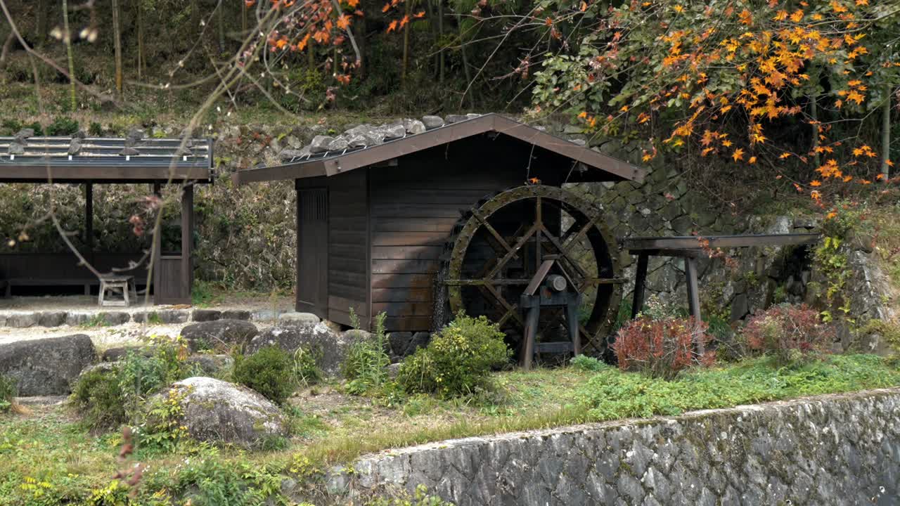 A stunning view of a traditional water mill along the historic Nakasendo Trail in Japan, surrounded by vibrant red autumn foliage.