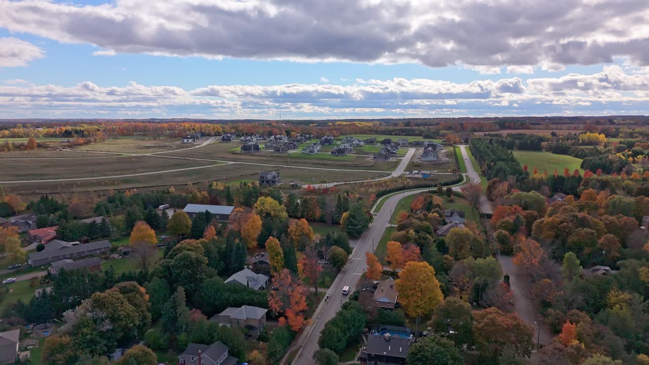 Ripresa aerea con drone di un nuovo complesso residenziale vicino ad Alton, Caledon, Ontario, con strade sinuose, alberi autunnali e nuvole suggestive, che mostra l'espansione suburbana