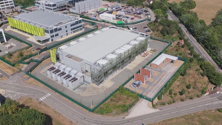Perspectiva de ângulo alto de um edifício de Data Center industrial mostrando o terreno complexo com estradas e árvores ao redor durante uma tarde ensolarada e brilhante