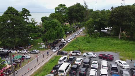 aerial: drone travels above the packed parking zone with cars to the busy road, people wait in queue to be transported by ferry from the koh chang island to mainland of trat, thailand, asia