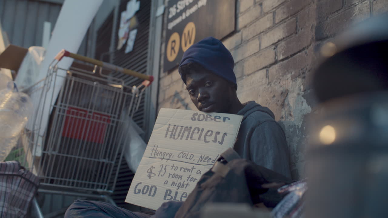 Portrait of Homeless Black Man Holding Handwritten Sign in City Alley