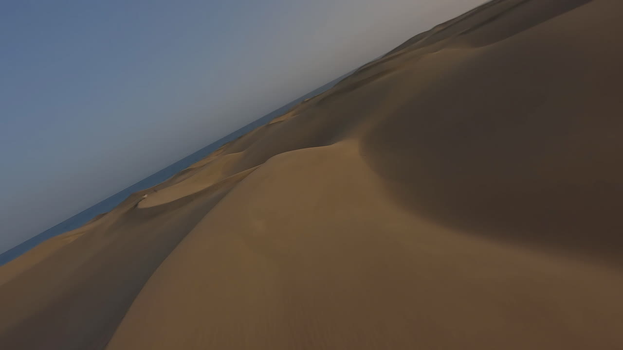 vuelo aéreo rápido y bajo sobre dunas de arena hacia el mar al atardecer, maspalomas