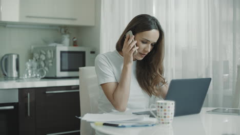 Mujer-Joven-Llama-Al-Teléfono-En-La-Cocina-De-Casa.-Mujer-De-Negocios-Hablando-Por-Teléfono-Móvil