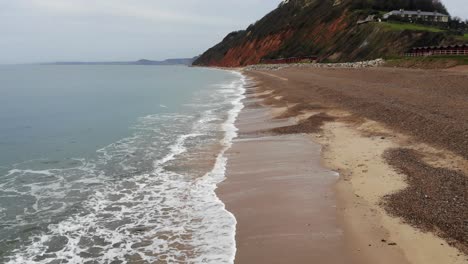 Erstaunliche-4K-Luftaufnahme,-Die-Entlang-Der-Küste-über-Den-Rollenden-Wellen-Des-Britischen-Strandes-Von-Branscombe-Fliegt