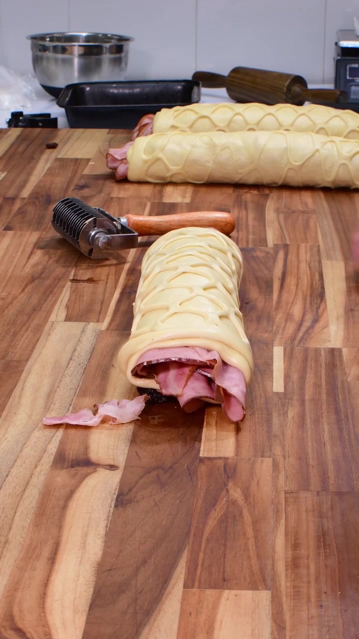 Primo piano di un fornaio che usa un tagliapasta a reticolo per il rotolo di pane al prosciutto