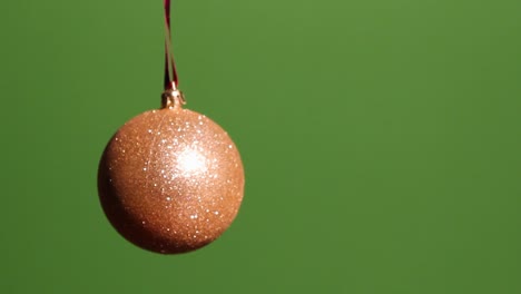 Gold-sphere-ornament-with-red-ribbon-spins-back-and-forth-on-its-axis-in-front-of-a-green-screen