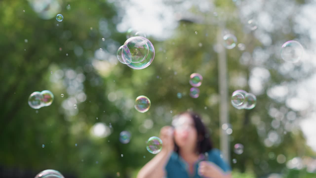 Kadın etrafında yumuşak odaklı park baloncukları, sessiz kaldırım ve yeşil ağaçlar, kenarda park etmiş bisiklet, bokeh içinde süzülen hayalperest odaksız sabun küreleri, yalnız başına keyif ve bilinçli oyun, nostaljik yavaşlık
