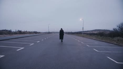 a woman walking down an empty parking lot during a foggy morning