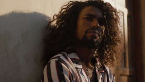 cool and mysteriously looking black arabic man leans against the wall of an old house wall during golden hour.