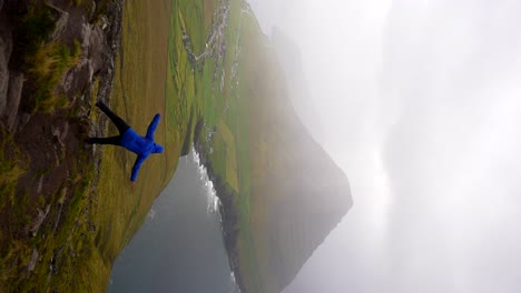 hombre con chaqueta azul balanceándose en una roca en vidoy, islas feroe