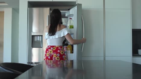 tracking shot of girl walking to fridge and taking something out