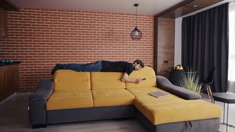 a man lays on sofa's rib, looking to a cell phone