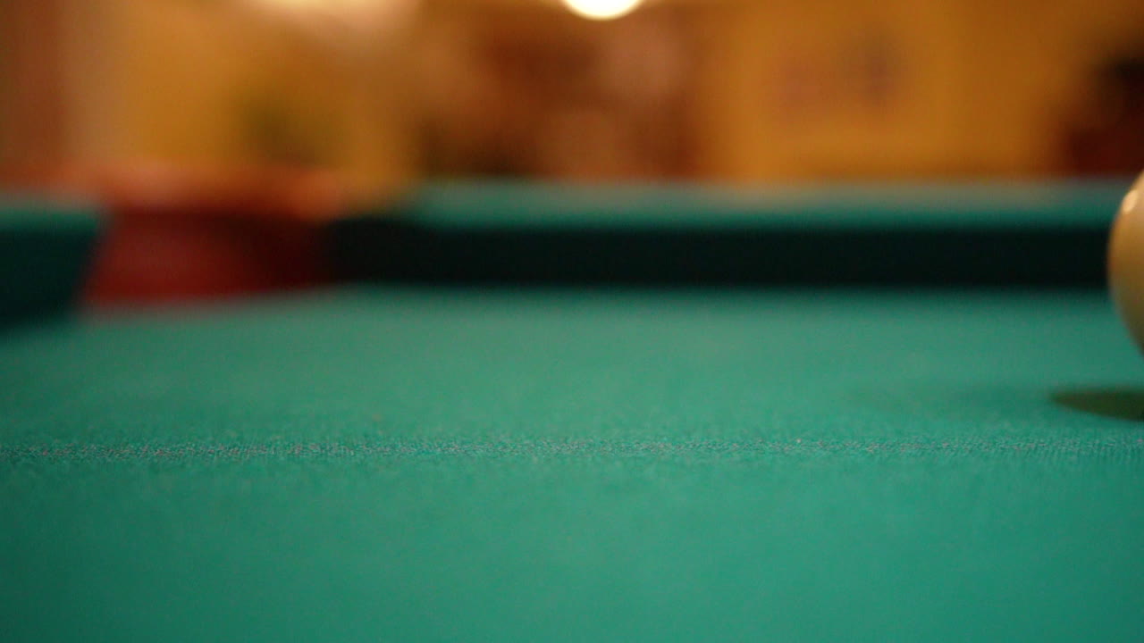 Slow Motion Billiards solid black 8 ball shot in corner pocket on pool table with green felt and brown pockets with the cue ball sliding out of frame Low Angle Close Up with Red Spinning Dots