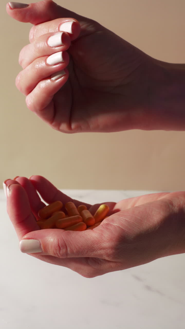 Yellow multivitamin and Coenzyme Q10 capsules softly fall from one hand to another in a calm, minimal setting with warm lighting, emphasizing wellness and daily supplement routines.