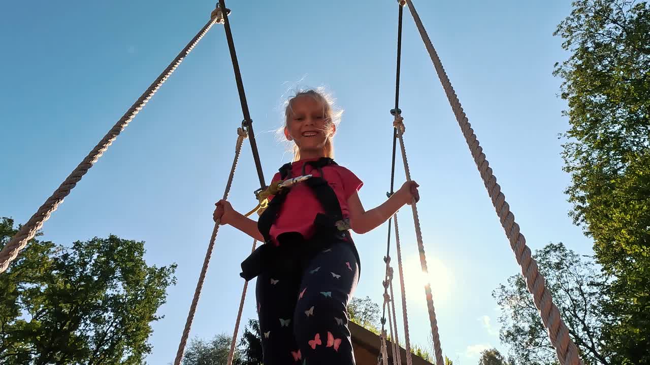 niña feliz jugando en la atracción de tarzán en el patio de recreo en el parque de atracciones