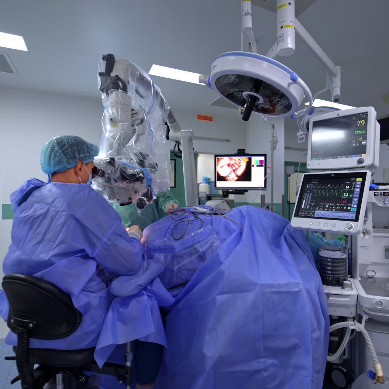Neurosurgery performed in modern well-equipped surgical theatre. Doctor sits near the patient looking at microscope