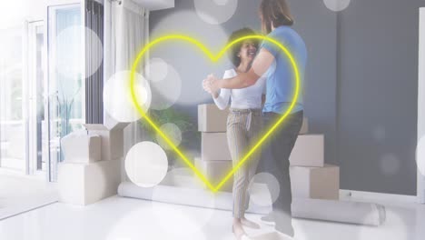 animación de corazón de neón amarillo y manchas blancas sobre una feliz pareja diversa bailando entre cajas de embalaje