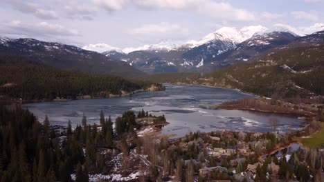 aerial drone shot green lake and snowy mountains in whistler, canada