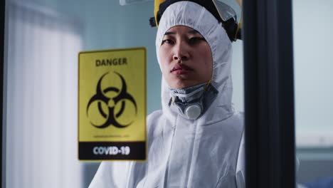 healthcare worker in hazmat suit behind covid-19 biohazard sign