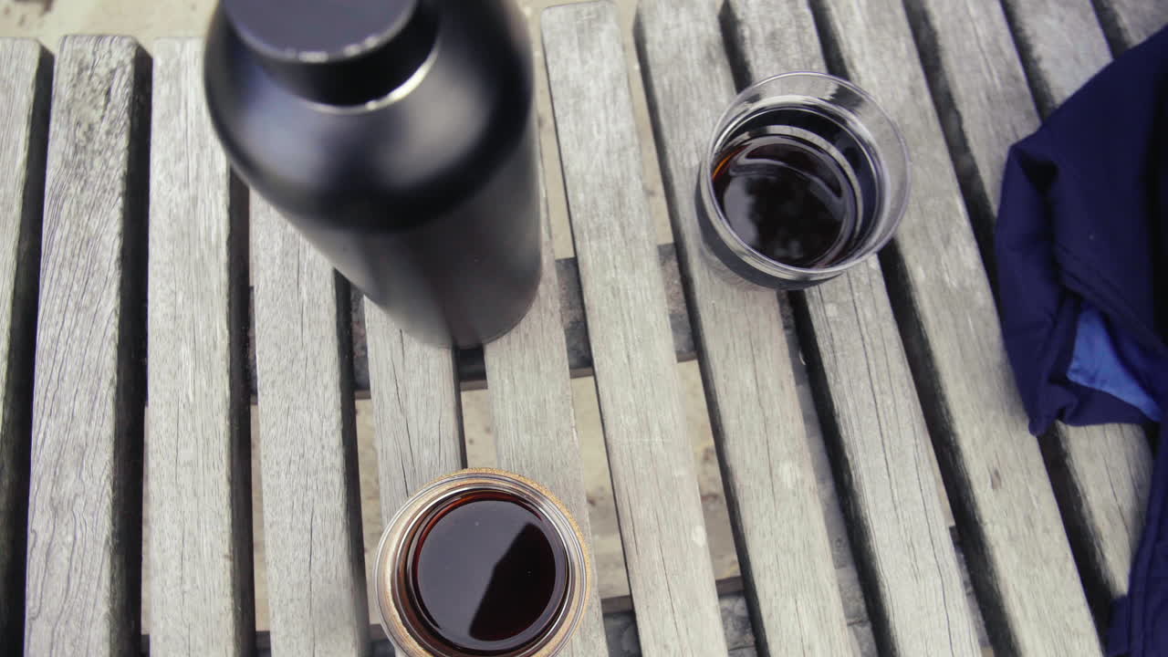 dos tazas con café caliente y un termo en un banco de madera en la playa en un día frío