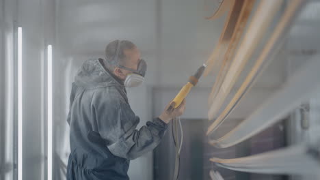 A-man-in-a-protective-suit-and-mask-sprays-paint-through-a-spray-gun-in-slow-motion-on-steel-parts.