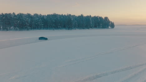 car drifting fast corners on snowy norbotten woodland ice track at sunset, aerial view