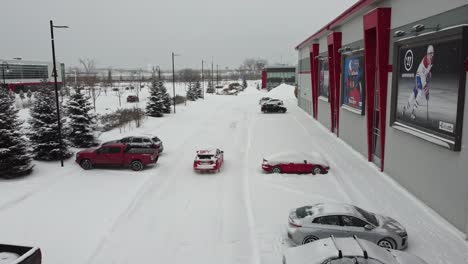 Erleben-Sie-Die-Atemberaubende-Aussicht-Einer-Drohne,-Die-In-Einer-Ruhigen-Winterlandschaft-über-Einem-Roten-Auto-Auf-Einem-Schneebedeckten-Parkplatz-Fliegt