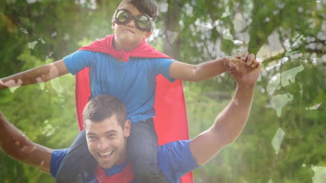 animation of foliage over happy caucasian father and son having fun dressed like superheroes