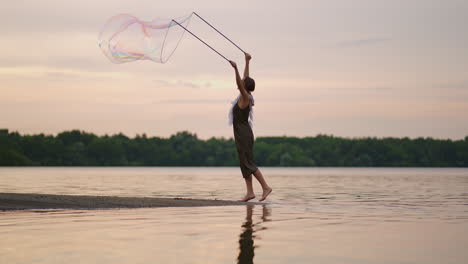 a young girl artist shows magic tricks using huge soap bubbles. create soap bubbles using sticks and rope at sunset to show a theatrical circus show