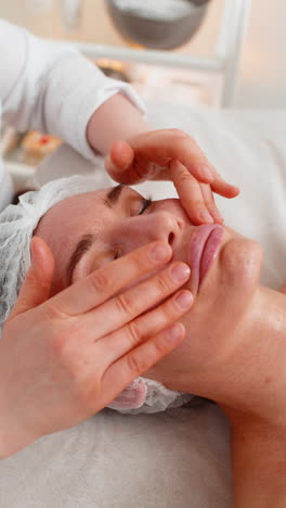 esteticista aplicando una máscara de crema hidratante química médica en el rostro de una mujer joven adulta
