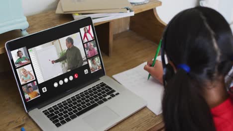 Schoolgirl-using-laptop-for-online-lesson-at-home,-with-diverse-teacher-and-class-on-screen