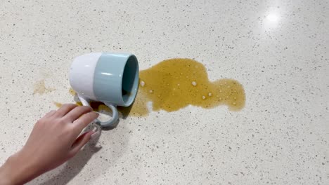 a hand accidentally spills coffee from a mug onto a kitchen countertop, creating a mess in bright lighting